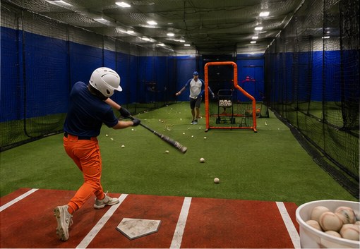 Young hitter finishing his swing in the NVBA indoor batting cage with a coach behind the L-screen