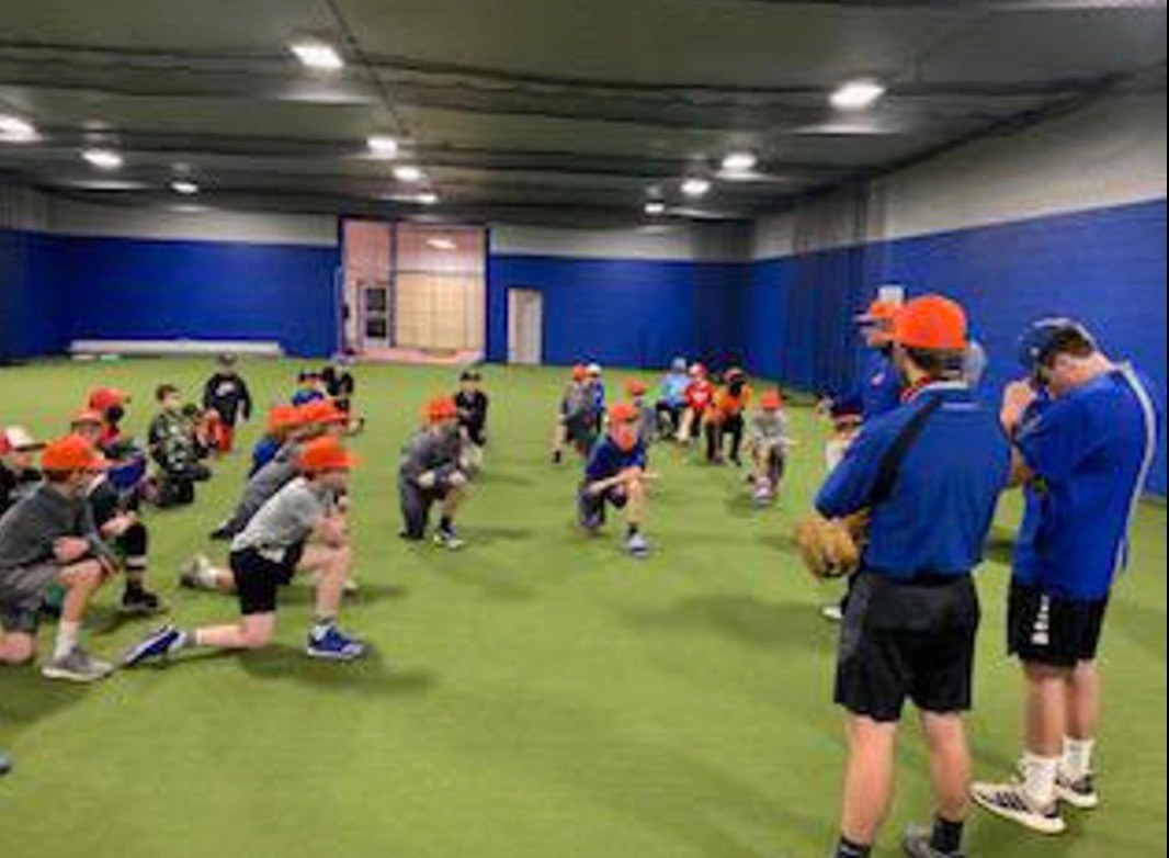 Large group of young NV Stars players taking a knee on the indoor turf while two coaches address the team